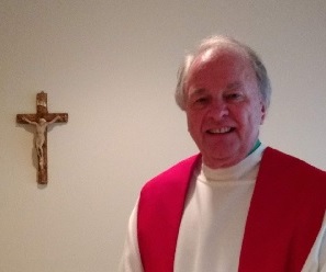 A portrait of Fr Larry Hansen dressed in white alb and red stole next to a crucifix