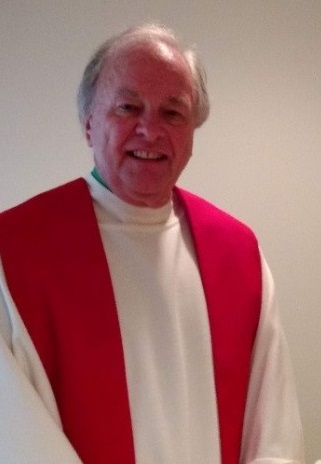 Portrait of Fr. Hansen, smiling, wearing a white alb and red stole