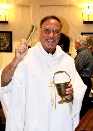 Portrait of Fr. Ray, smiling, wearing a white chasuble while sprinkling holy water